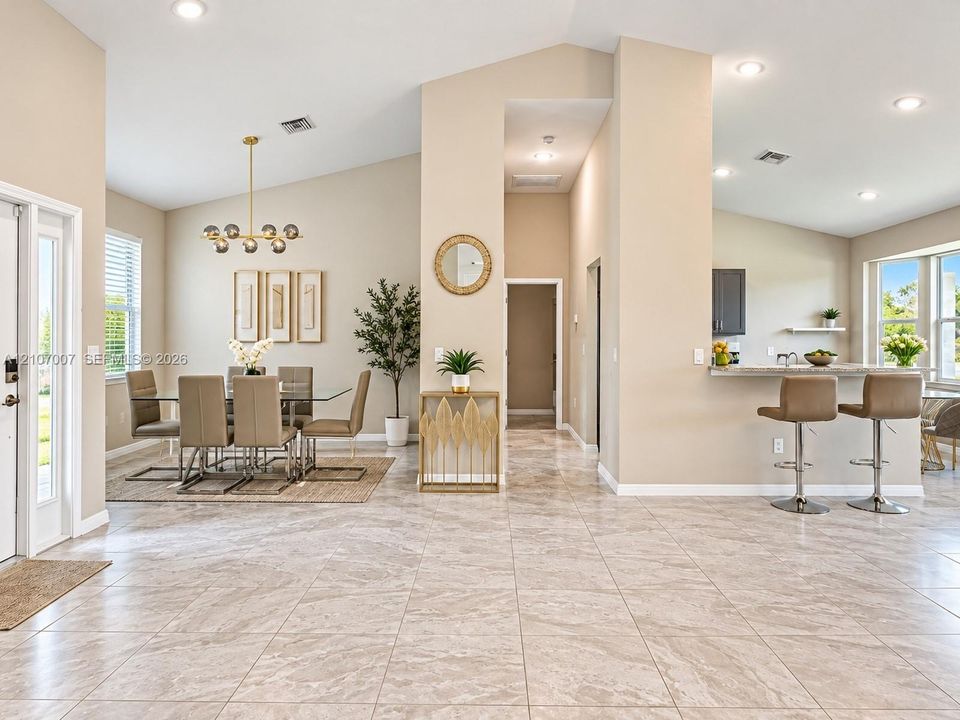 Open-concept interior featuring vaulted ceilings, oversized tile flooring, recessed lighting, a modern multi-light chandelier, and a kitchen peninsula with bar seating