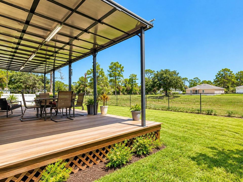 Covered outdoor deck featuring wood-finish decking, a translucent roof structure, lattice skirting, and a fenced-in grassy yard