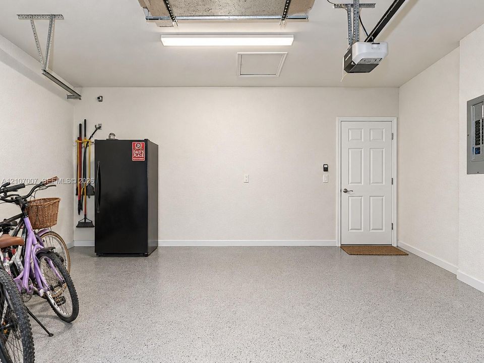 Finished garage space featuring epoxy-coated flooring, neutral wall finishes, integrated linear lighting, and a six-panel entry door