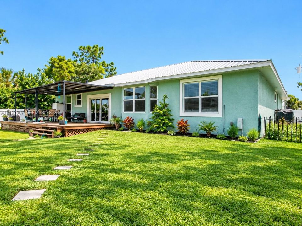 Stucco exterior featuring a metal roof, covered wood deck, sliding glass doors, and a landscaped lawn with stone pavers