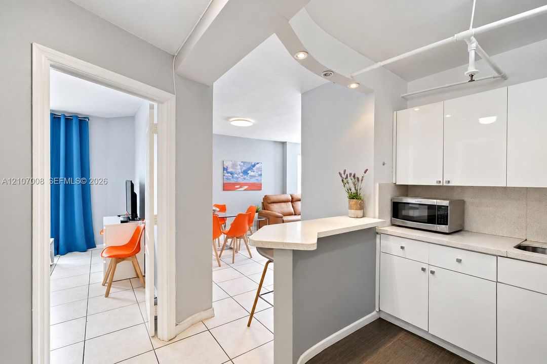 Kitchen featuring high-gloss white cabinetry, stone-finish countertops, a breakfast bar, recessed lighting, and tile flooring