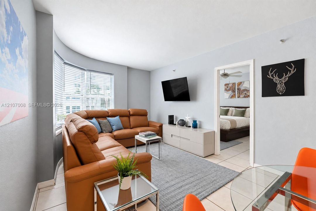 Living space featuring neutral ceramic tile flooring and a multi-panel bay window with horizontal blinds