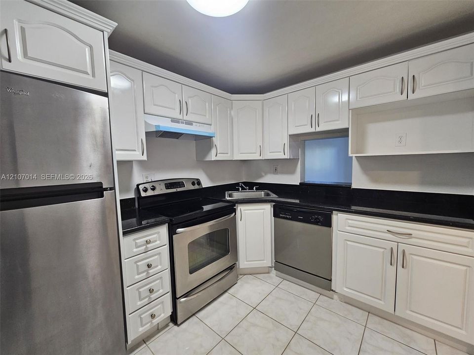 White cabinetry, black countertops, stainless steel appliances, and tiled flooring