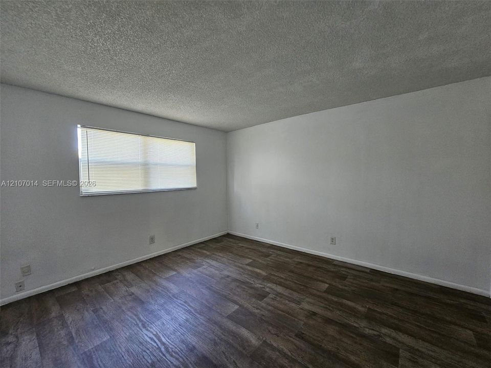 Interior space featuring neutral wall paint, wood-finish flooring, a textured ceiling, and a window with horizontal blinds