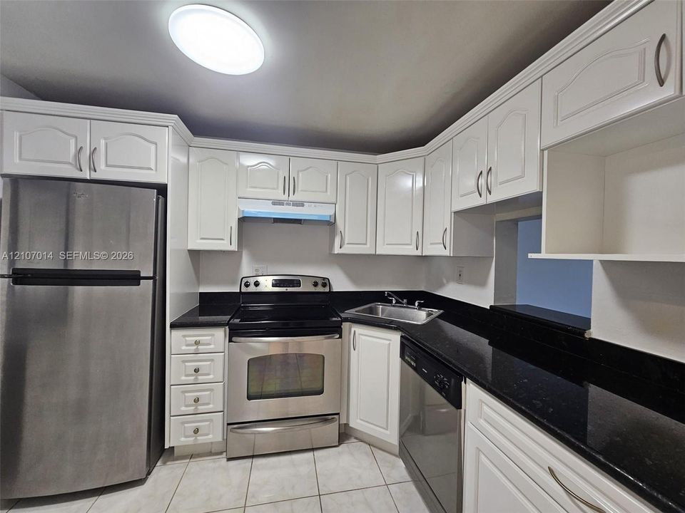 Kitchen featuring white raised-panel cabinetry, dark solid-surface countertops, stainless steel appliances, ceramic tile flooring, and a flush-mount ceiling fixture