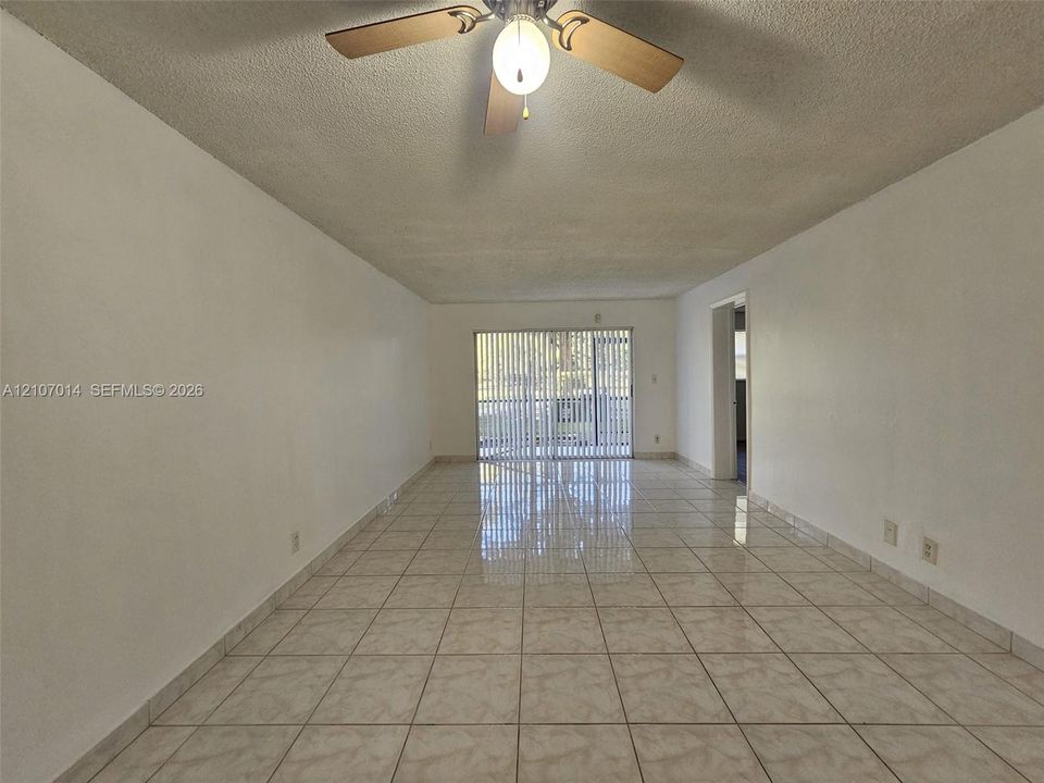 Interior space featuring neutral tile flooring, a central ceiling fan with integrated lighting, and glass sliding doors
