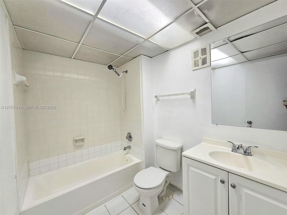 Bathroom featuring a vanity with integrated sink, drop-in soaking tub with a tiled surround, wall-mounted mirror, and tile flooring