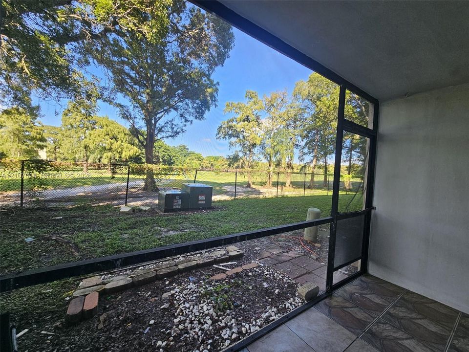 Screened-in porch featuring tiled flooring, a decorative stone border, and expansive outdoor grounds with mature trees