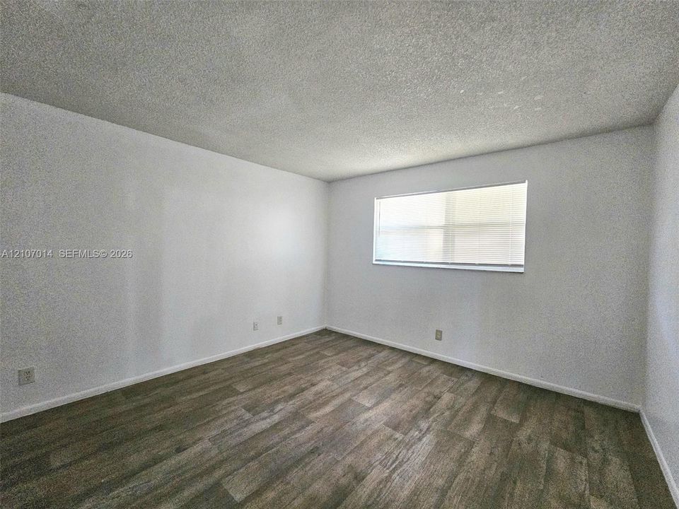 Interior room featuring white-painted walls, wood-finish flooring, and a single horizontal window with integrated blinds