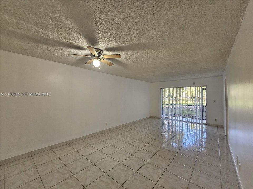 Spacious interior featuring light-colored tile flooring, a multi-blade ceiling fan, and sliding glass doors with vertical blinds