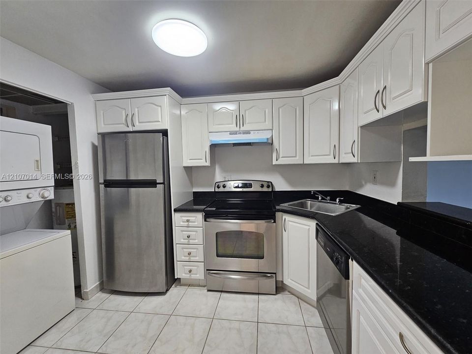 Kitchen featuring white cabinetry, contrasting dark stone countertops, stainless steel appliances, and tiled flooring