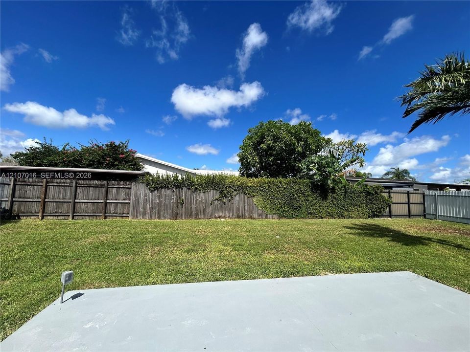 Backyard featuring a concrete patio, wood privacy fencing, and perimeter hedging on one side