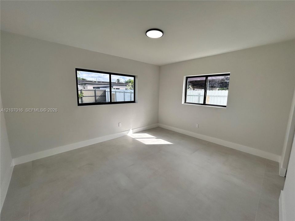 Neutral interior space featuring large-format tile flooring, dual-pane windows with black frames, and a flush-mount LED ceiling light