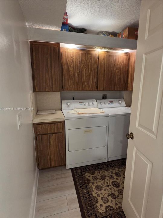 Laundry area featuring wood-finish cabinetry, neutral solid-surface countertop, and light-tone plank flooring
