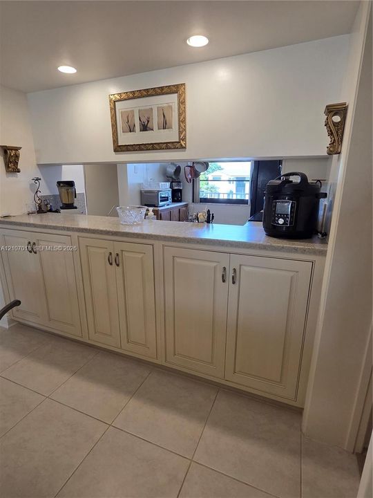 Built-in cabinetry with off-white panel doors, neutral solid-surface countertop, recessed ceiling lighting, and large-format ceramic tile flooring