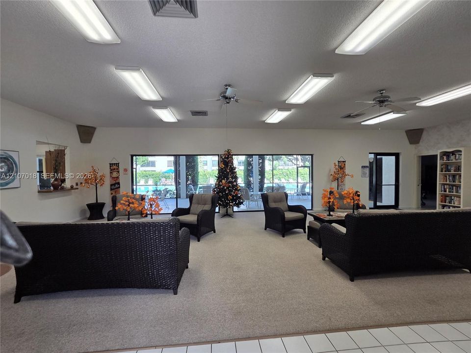 Common area featuring wall-to-wall carpeting, multiple ceiling-mounted fluorescent light fixtures, ceiling fans, built-in shelving, and floor-to-ceiling windows