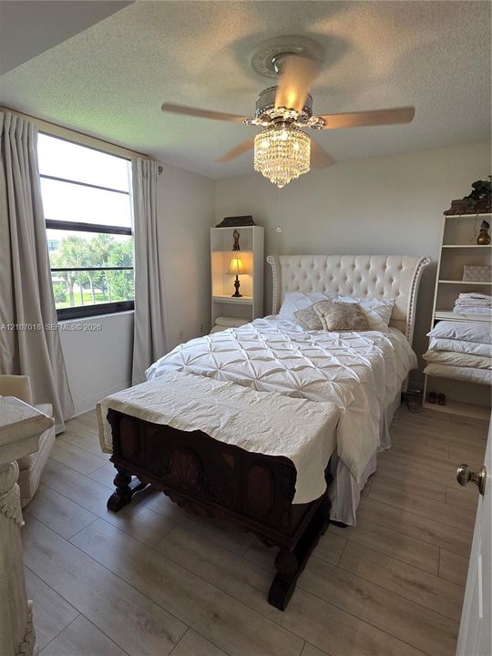 Wood-finish flooring, large-format window with dark trim, and a ceiling-mounted crystal chandelier fan