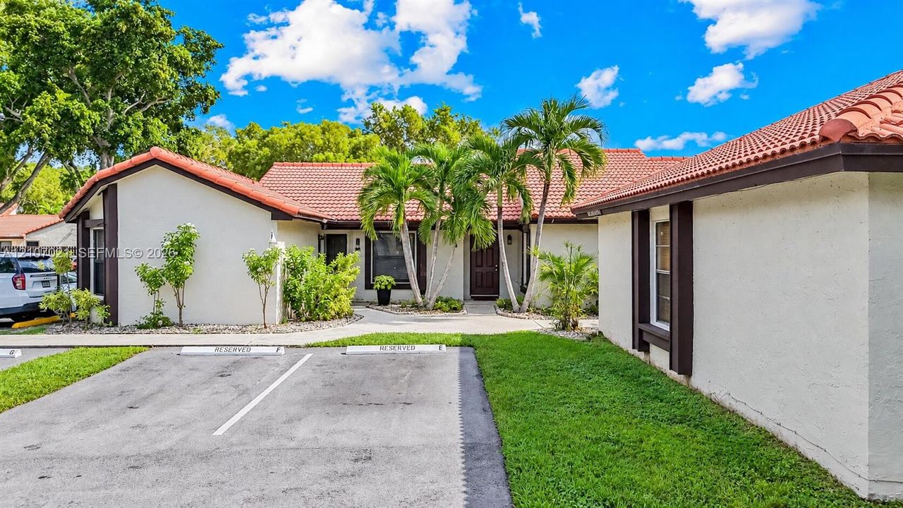 Stucco exterior featuring a terracotta tile roof, designated parking spaces, and mature palm landscaping