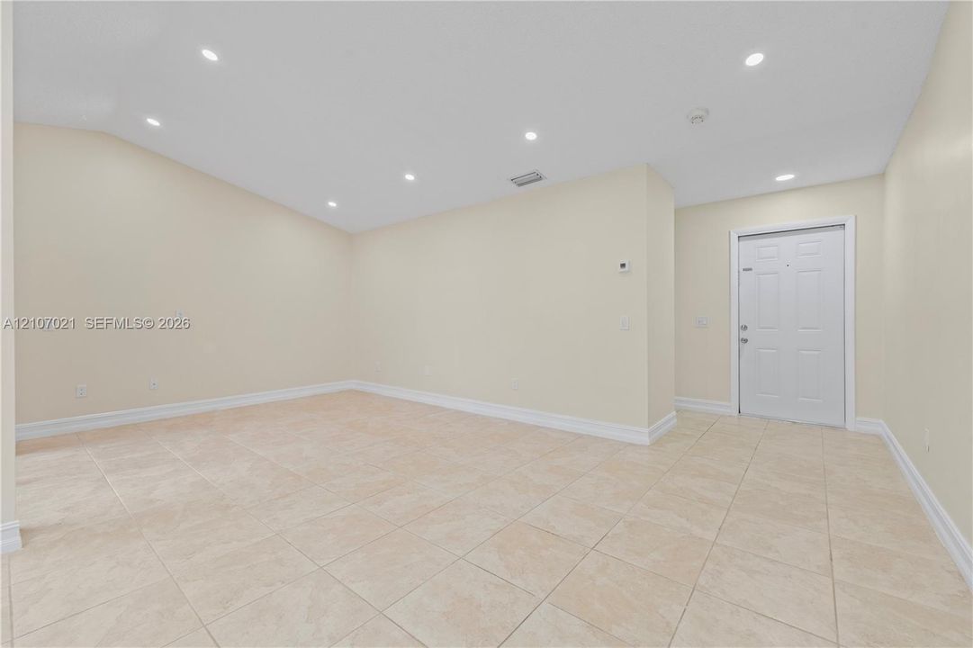Neutral-toned interior room featuring large-format ceramic tile flooring, recessed ceiling lighting, and a six-panel exterior entry door