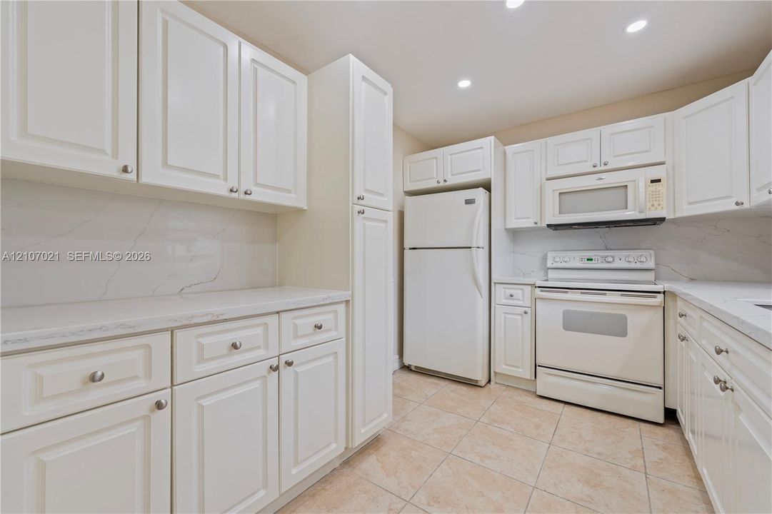 Kitchen featuring white shaker-style cabinetry, stone-surface countertops, stone-pattern backsplash, recessed lighting, and tile flooring