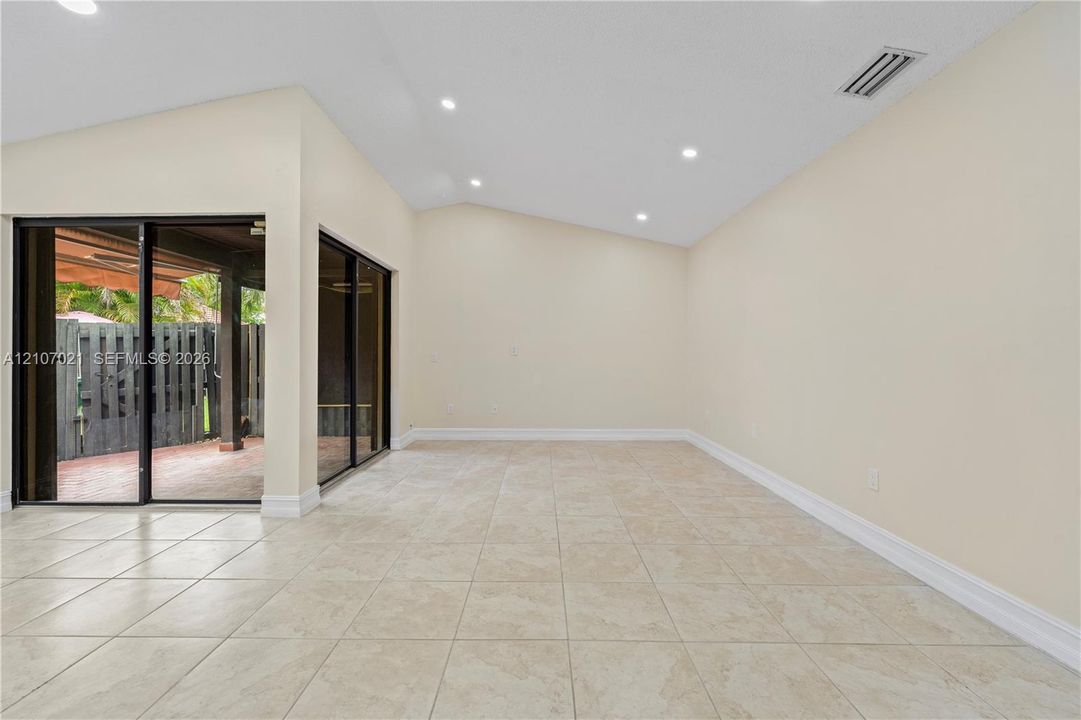 Vaulted ceilings, recessed lighting, tile flooring, and dual glass sliding doors opening to a covered patio