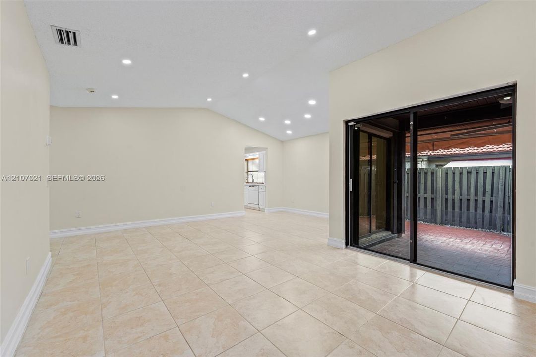 Living area featuring vaulted ceilings, recessed lighting, tile flooring, and oversized sliding glass doors opening to a paved patio