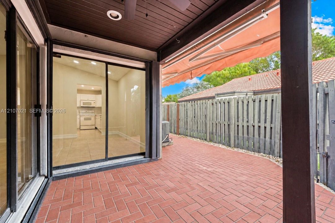 Covered patio featuring a herringbone-pattern brick floor, recessed ceiling lighting, a retractable awning, and sliding glass doors