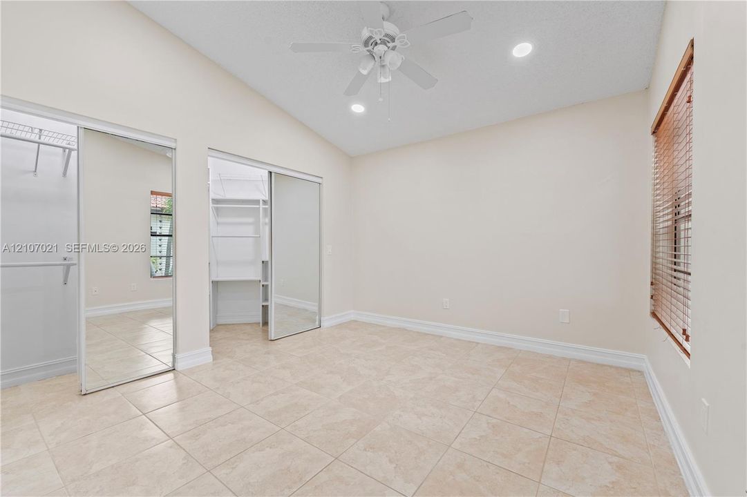Vaulted ceiling with a central fan, ceramic tile flooring, and dual closets featuring mirrored sliding doors and built-in shelving