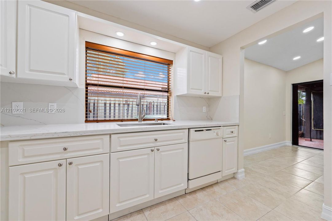 Kitchen featuring white shaker-style cabinetry, white countertops with grey veining, a stainless steel undermount sink with a gooseneck faucet, and integrated recessed lighting