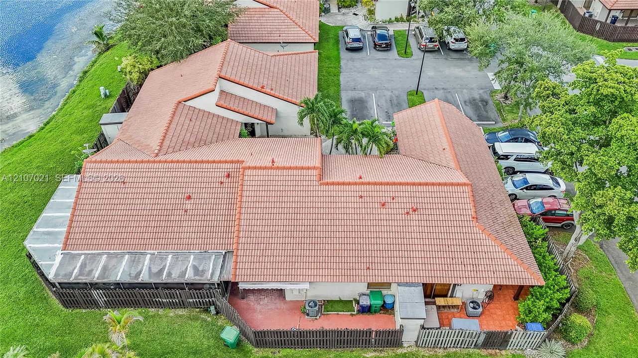 Aerial perspective of a multi-unit property featuring a red tile roof, waterfront location, covered patio, fenced outdoor space, and dedicated parking