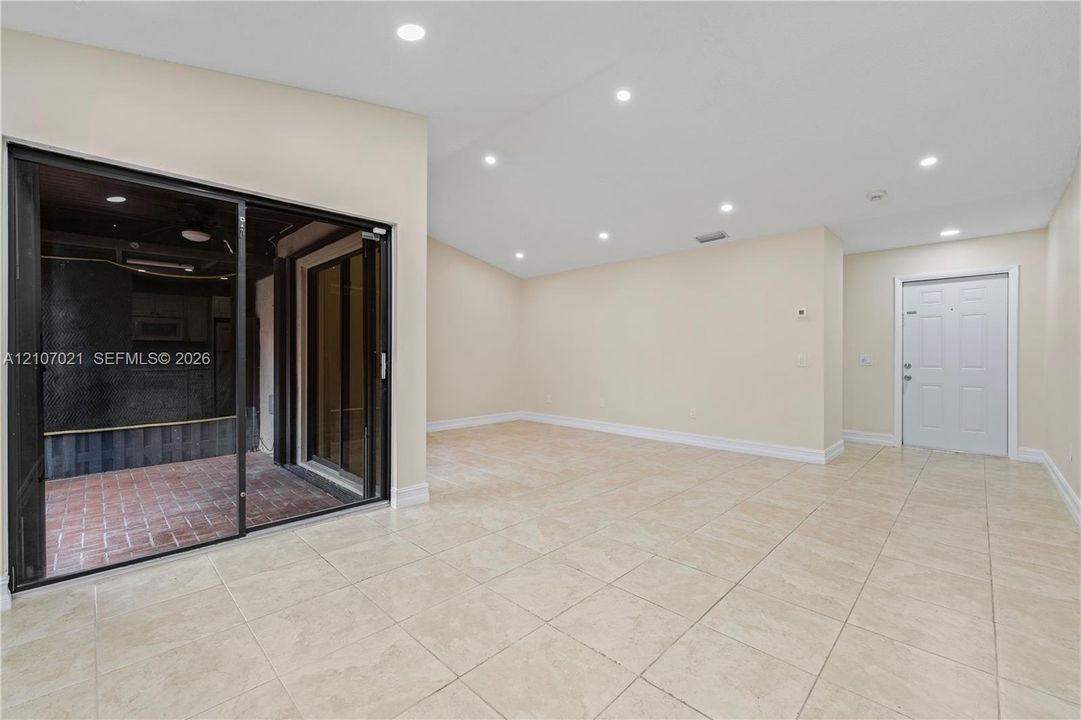 Large-format tile flooring, recessed ceiling lighting, sliding glass door with a black frame, and a white paneled entry door
