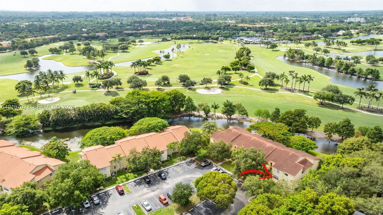Aerial perspective of multi-family residential building featuring a terracotta-style roof, surface parking area, and mature landscaping