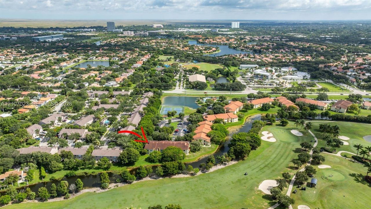 Aerial perspective of residential building with a tile roof, situated along a golf course featuring water hazards and manicured fairways