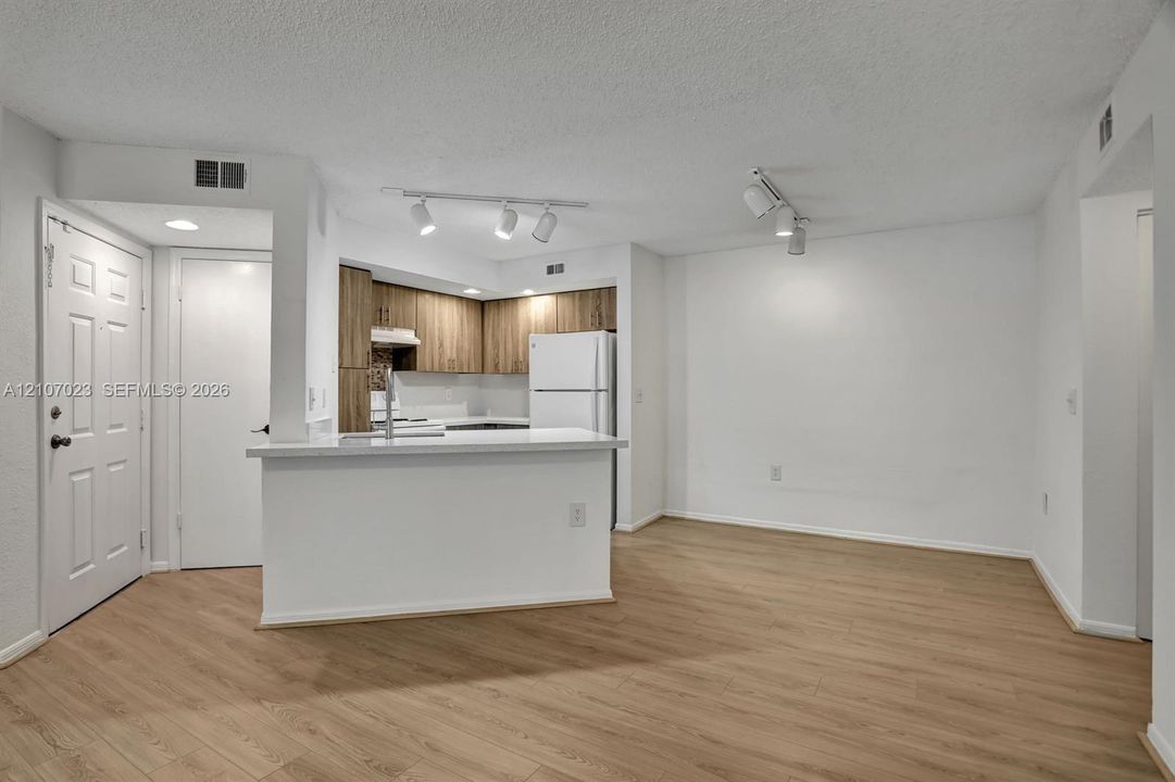 Kitchen featuring wood-finish cabinetry, white countertop, white appliances, wood-finish flooring, and multi-directional track lighting
