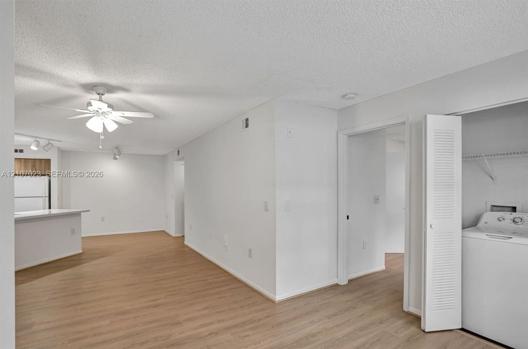 Open-concept interior featuring wood-finish flooring, a ceiling fan with integrated lighting, track lighting, and a laundry closet with louvered doors