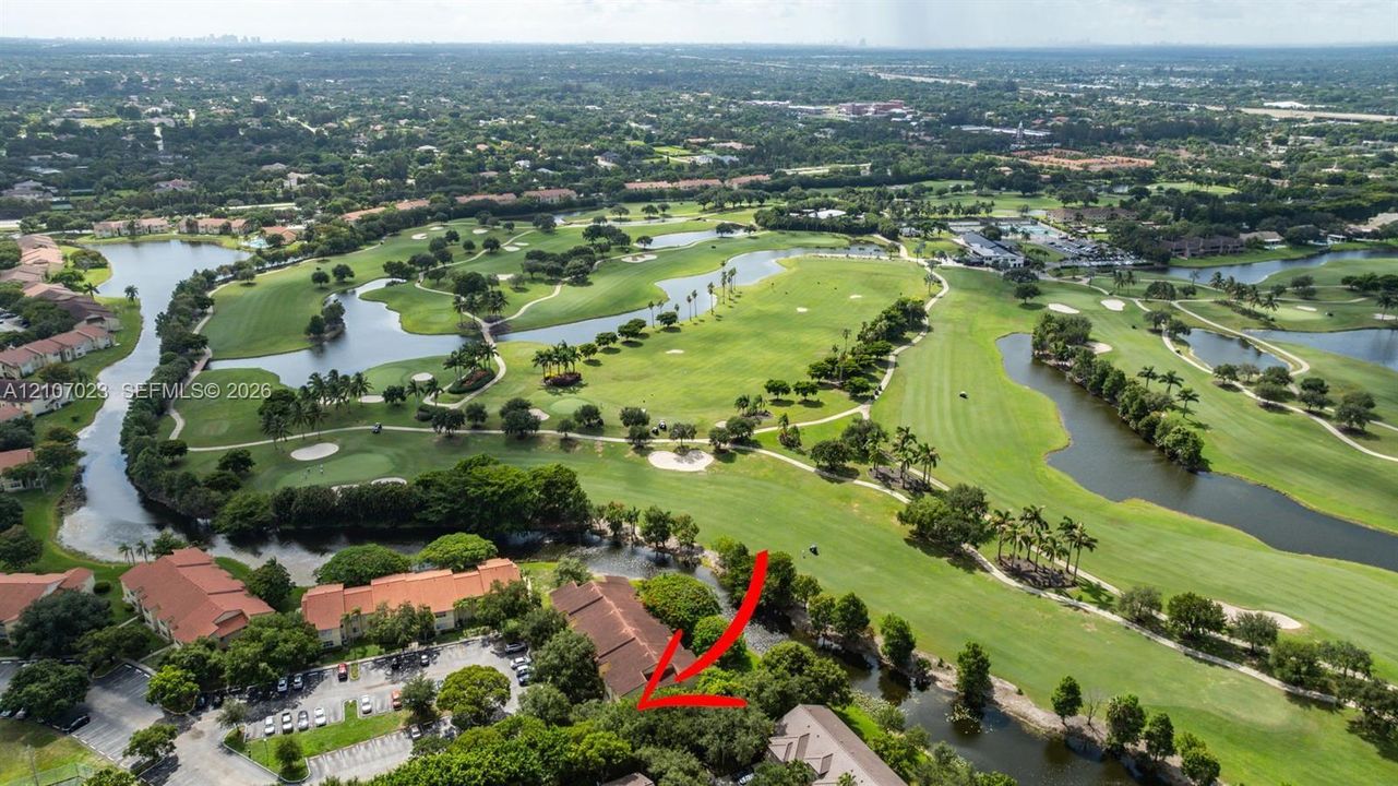 Aerial perspective featuring extensive manicured golf course grounds, integrated water features, mature tropical landscaping, and paved parking area
