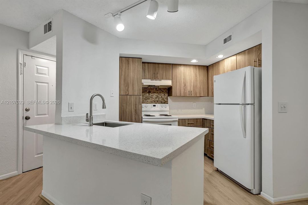 Kitchen featuring wood-finish cabinetry, white solid-surface countertops, wood-finish flooring, undermount sink with gooseneck faucet, and adjustable track lighting