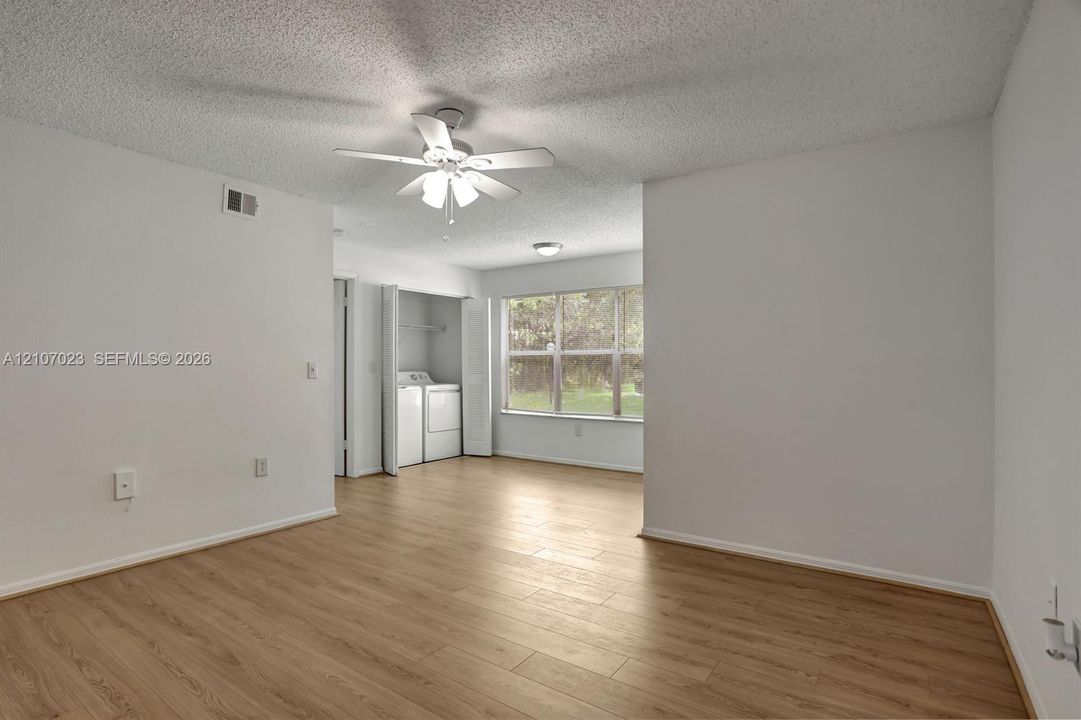 Wood-finish flooring, ceiling fan with integrated light fixture, large window, and enclosed laundry area