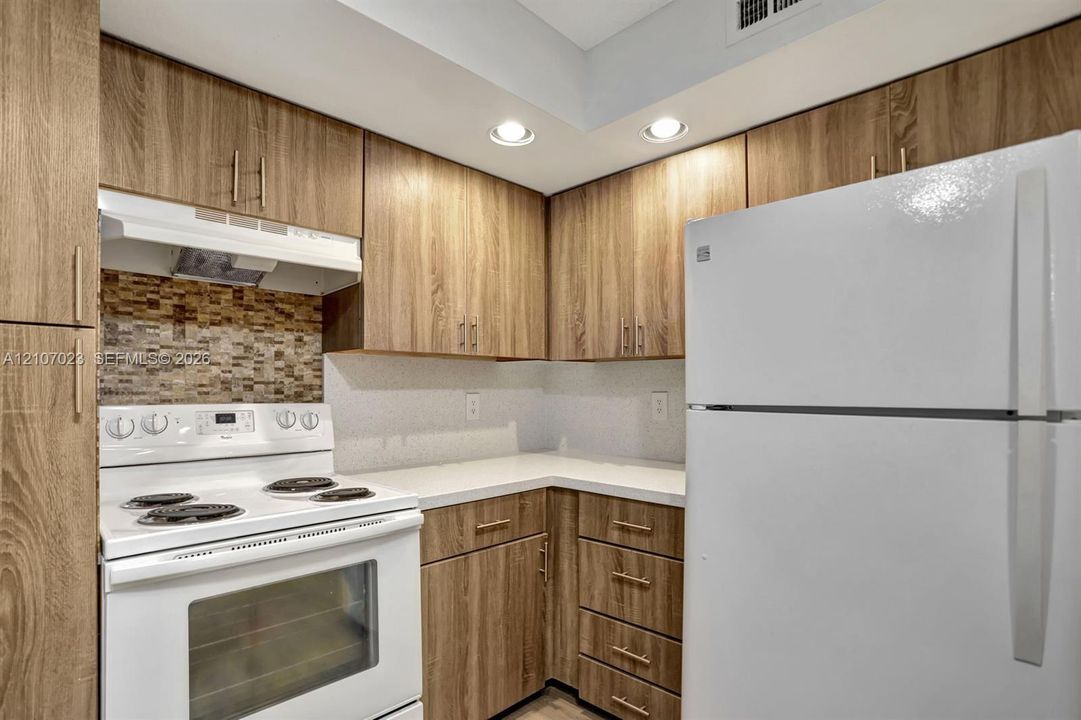 Kitchen featuring flat-panel wood-finish cabinetry, white countertops, mosaic tile backsplash, recessed ceiling lighting, and built-in appliances