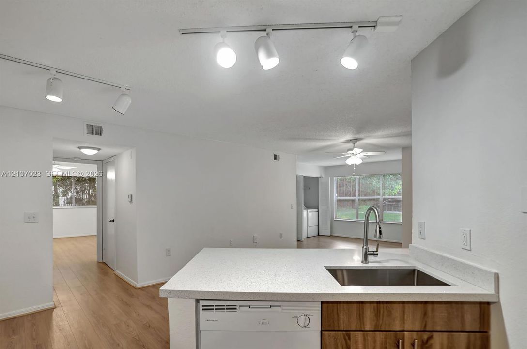 Kitchen featuring a stone-look countertop, stainless steel undermount sink with a gooseneck faucet, wood-finish cabinetry, built-in dishwasher, and adjustable track lighting