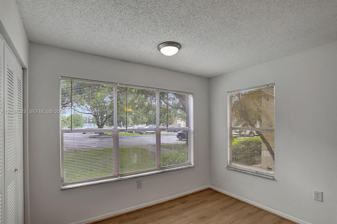 Room featuring wood-finish flooring, dual windows with blinds, a flush-mount light fixture, and floor-to-ceiling louvered closet doors