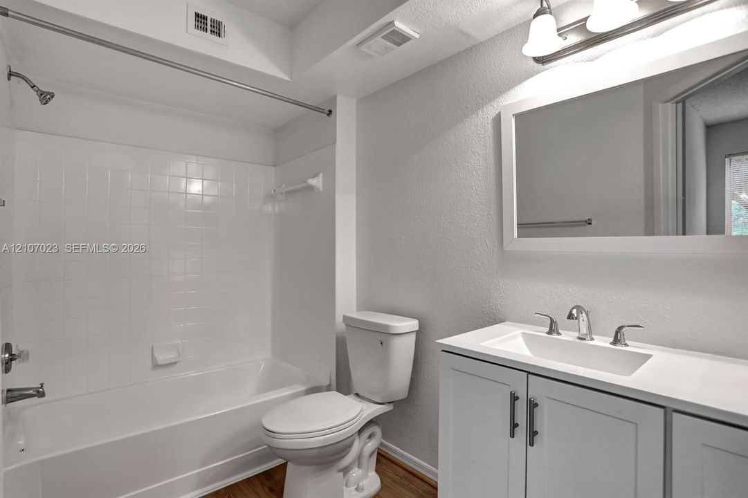 Bathroom featuring a white shaker-style vanity with a solid-surface countertop, an integrated sink, a tiled shower-and-tub combination, and a large framed vanity mirror