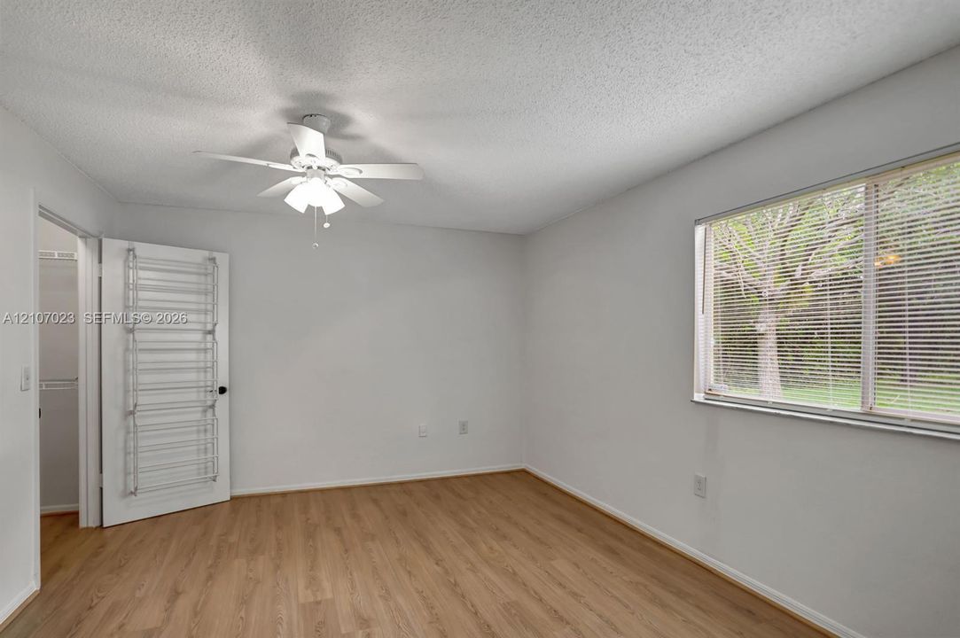 Room featuring wood-finish flooring, a white ceiling fan with integrated lighting, and a large window with horizontal blinds