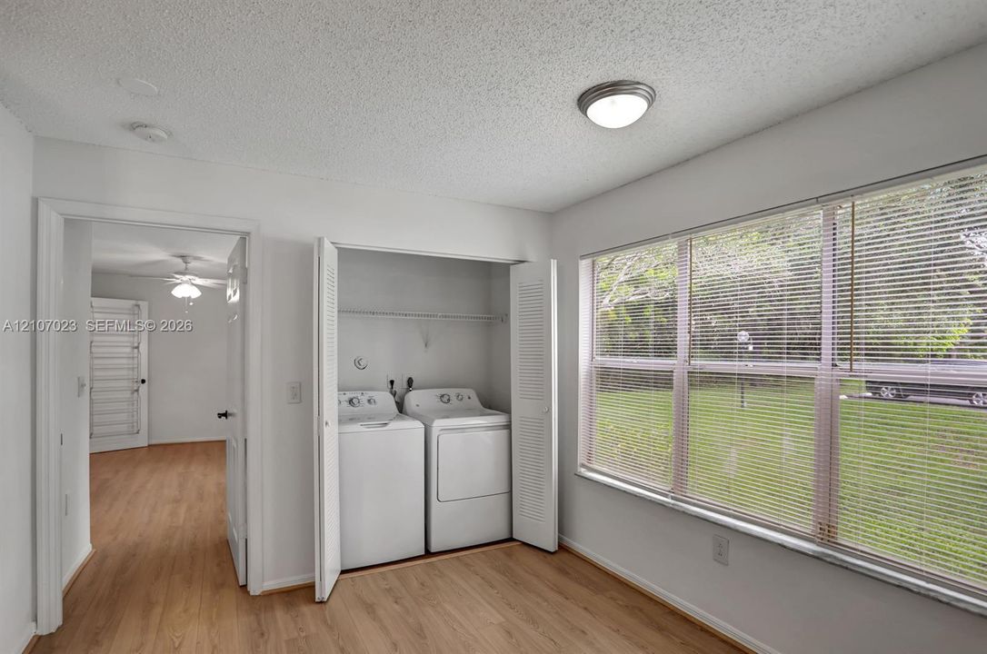 Laundry area featuring built-in louvered closet doors, wood-finish flooring, ceiling-mounted light fixture, and a large window with slatted blinds