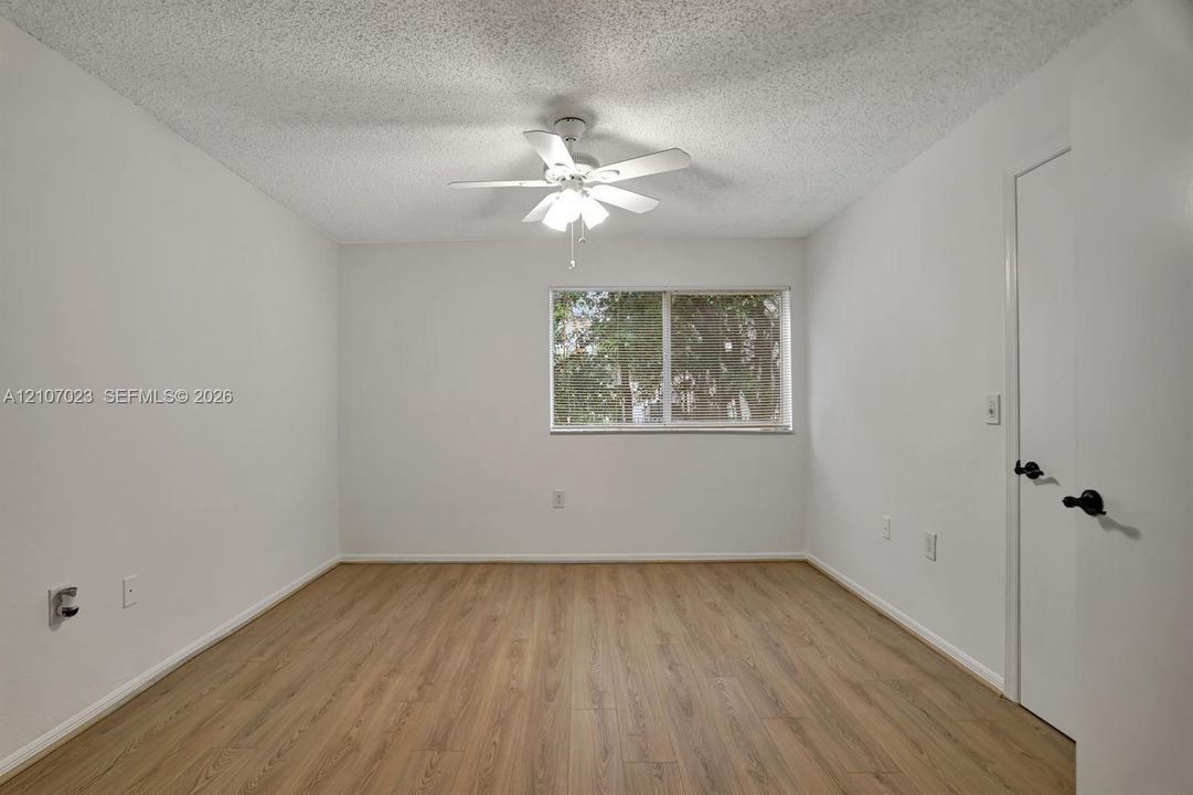 Neutral interior featuring wood-finish flooring, a ceiling fan with integrated lighting, a single-pane window, and a door with matte black hardware