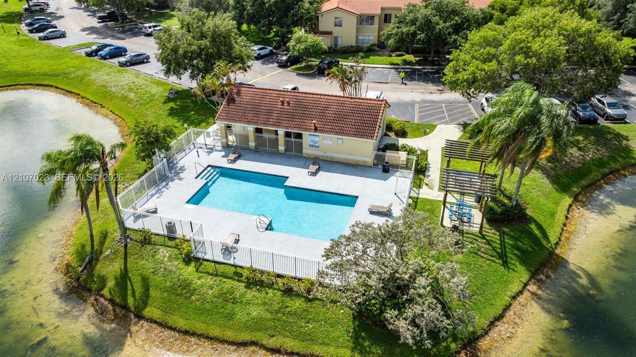Swimming pool with perimeter fencing, pool deck, cabana with tile roof, and pergola structure