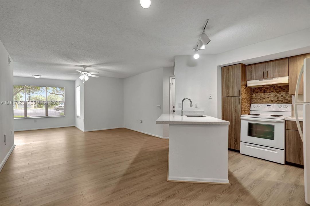Open-concept interior featuring wood-finish flooring, kitchen island with stone countertop, mosaic tile backsplash, wood-tone cabinetry, and multi-light track lighting
