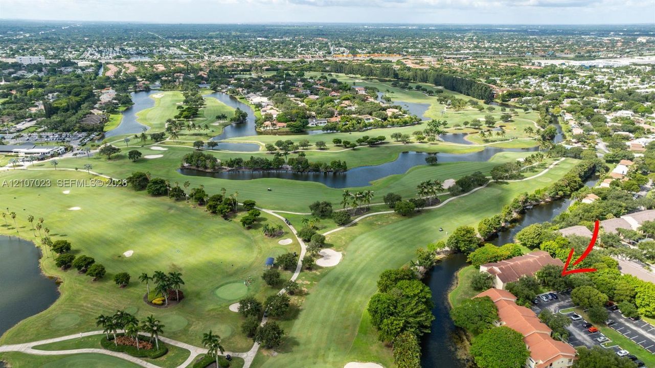 Aerial perspective of property featuring tile roofing, surface parking, and proximity to a golf course with water hazards and mature landscaping