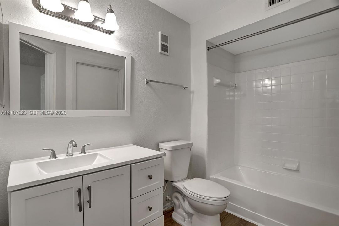 Bathroom featuring a white vanity with integrated sink, rectangular framed mirror, three-light fixture, and a tub-shower combination with full-height tile surround