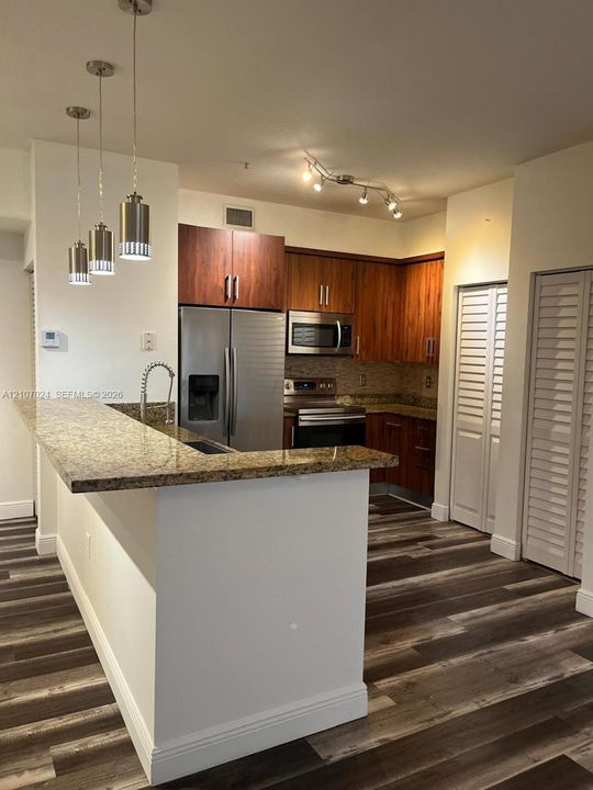 Kitchen featuring wood-finish cabinetry, stone-surface countertops, stainless steel appliances, wood-finish flooring, and multi-pendant lighting